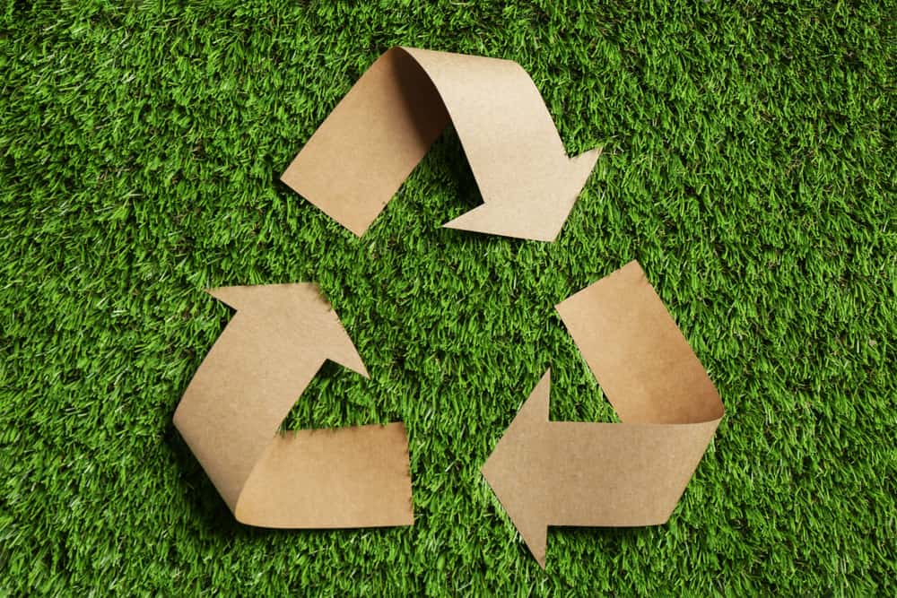 Recycling symbol cut out of brown paper sitting on grass